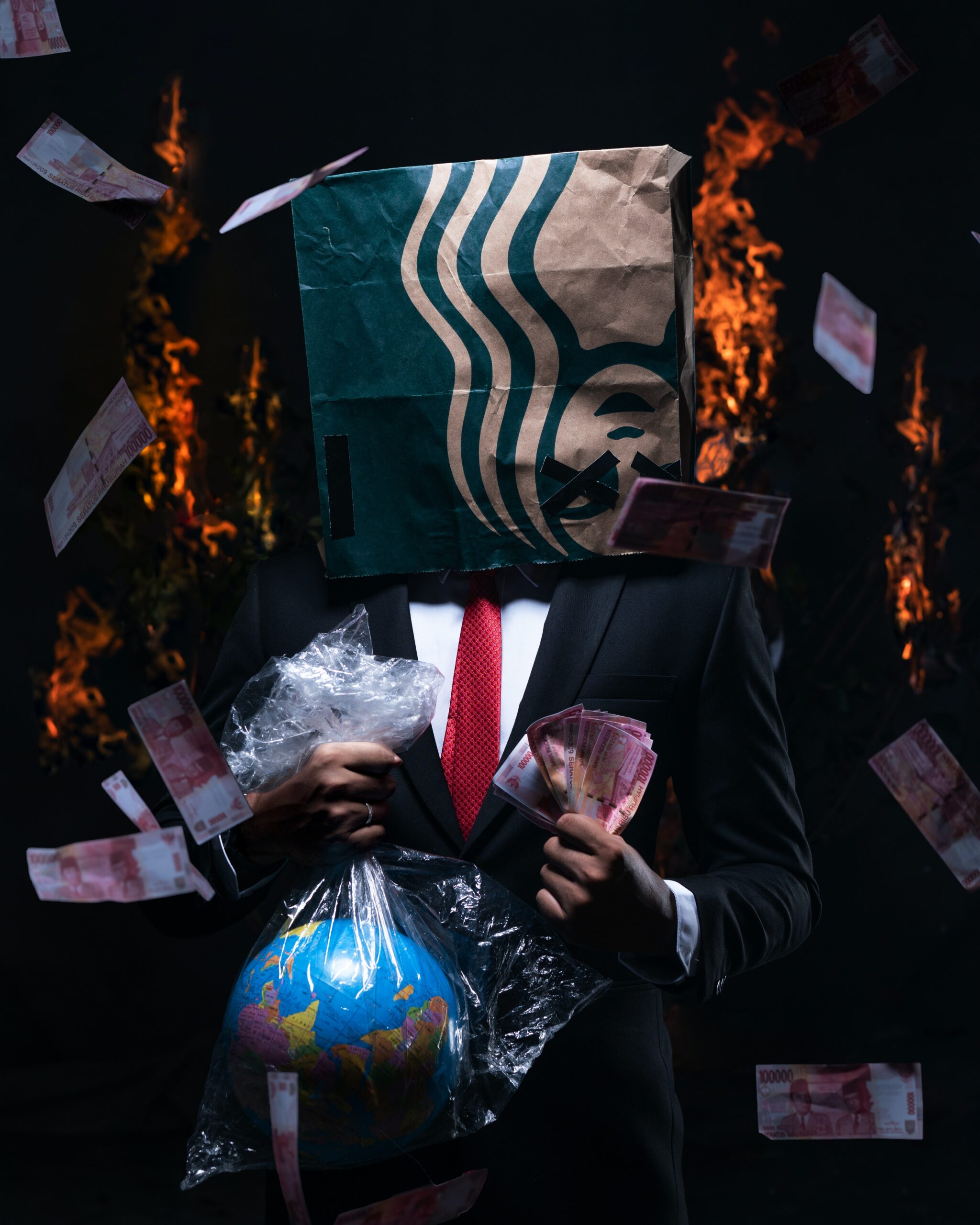person holding a globe in a plastic bag in one hand, wads of money in the other, and a Starbucks bag on head, while the background is in flames